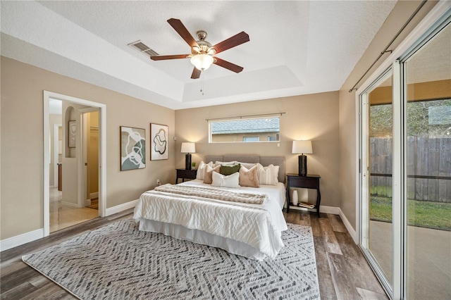 bedroom with access to exterior, ceiling fan, a raised ceiling, dark wood-type flooring, and a textured ceiling