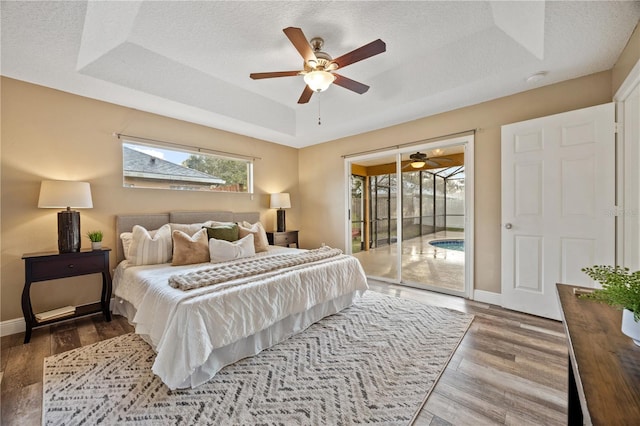 bedroom with wood-type flooring, access to outside, ceiling fan, a raised ceiling, and a textured ceiling