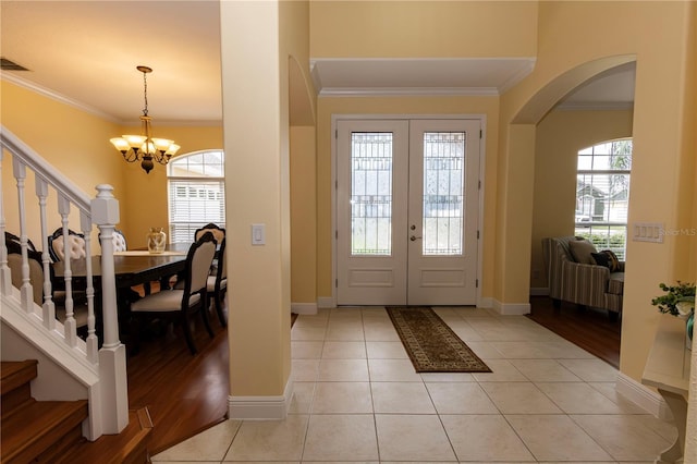 entryway with an inviting chandelier, light tile patterned floors, a wealth of natural light, and ornamental molding