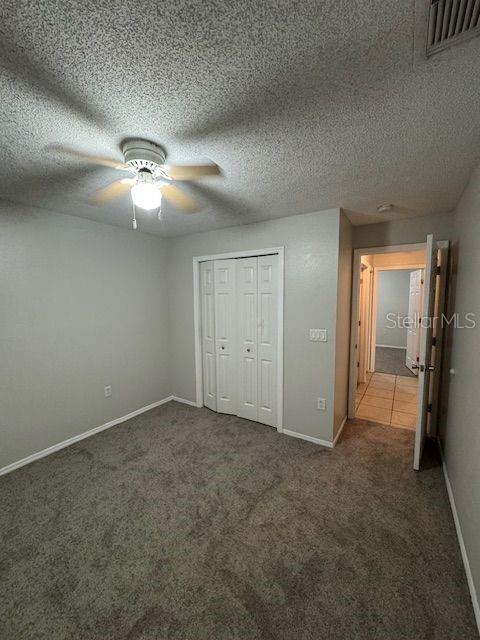 unfurnished bedroom with ceiling fan, a textured ceiling, carpet flooring, visible vents, and a closet