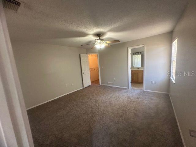 unfurnished bedroom with a textured ceiling, connected bathroom, carpet floors, visible vents, and a spacious closet