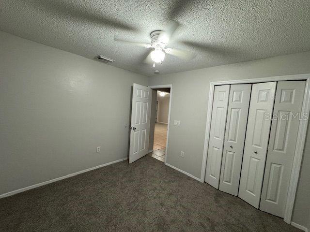 unfurnished bedroom featuring baseboards, visible vents, a textured ceiling, carpet flooring, and a closet