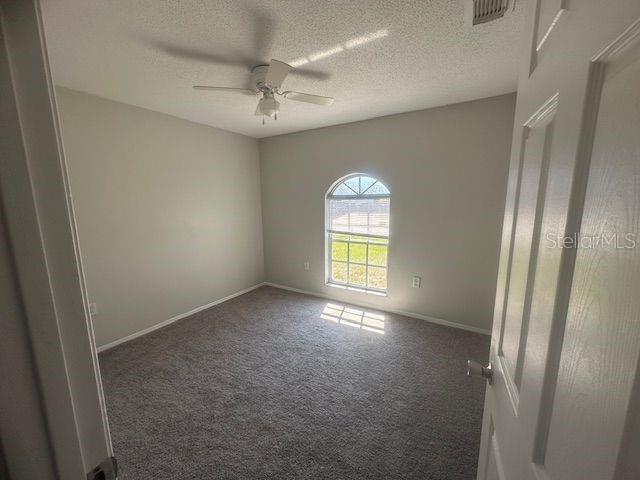 spare room featuring carpet, visible vents, ceiling fan, a textured ceiling, and baseboards