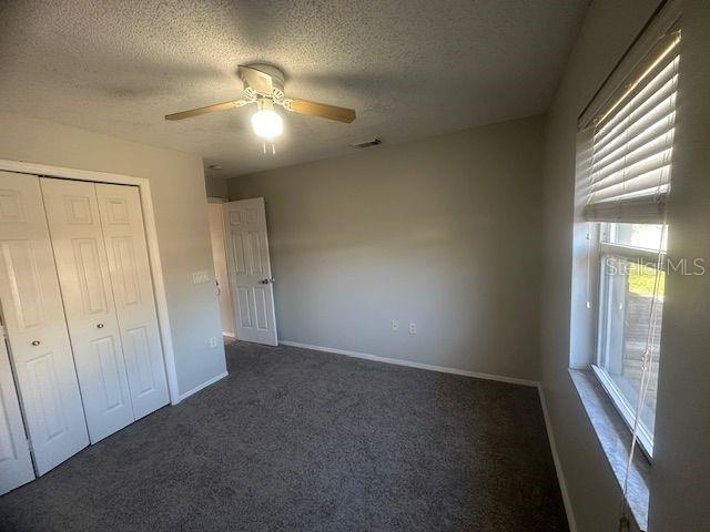 unfurnished bedroom with a textured ceiling, visible vents, baseboards, a closet, and dark colored carpet