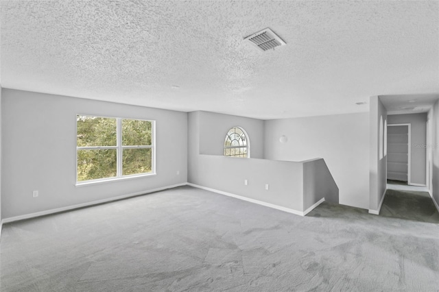 carpeted empty room featuring a textured ceiling, visible vents, and baseboards