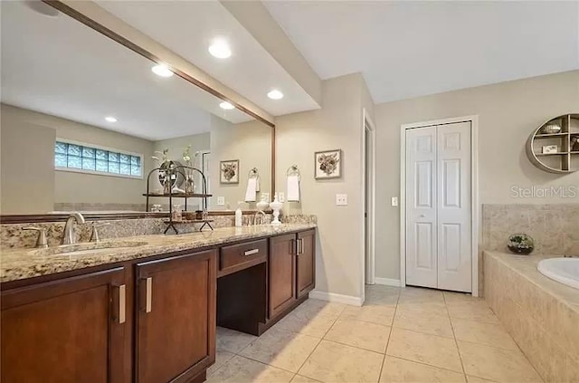 full bath featuring a relaxing tiled tub, double vanity, baseboards, tile patterned floors, and a sink