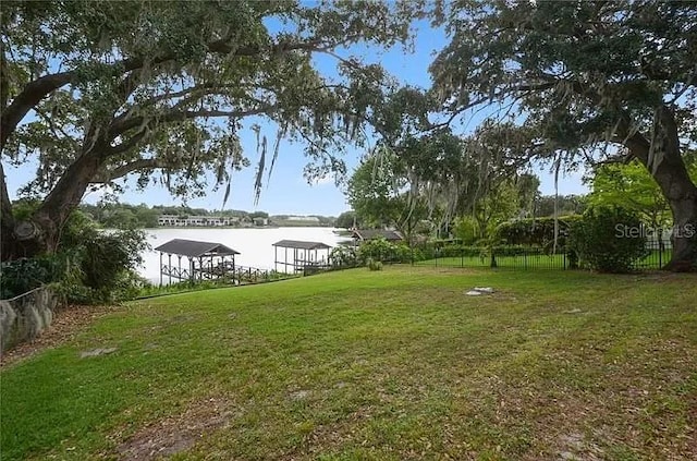 view of yard with a water view, fence, and a boat dock