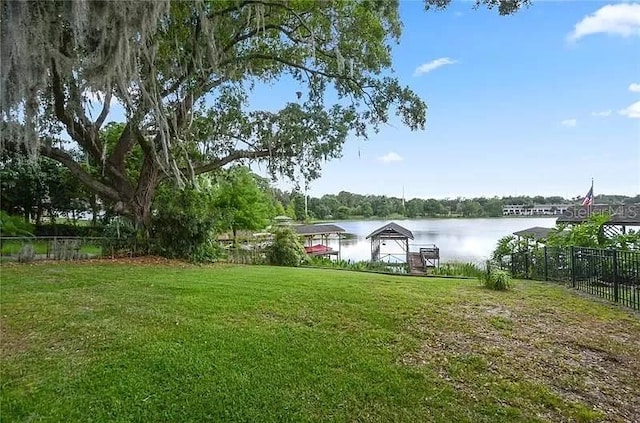 view of yard featuring a boat dock, a water view, and fence