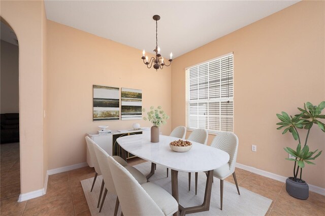 dining area with light tile patterned floors, baseboards, arched walkways, and a notable chandelier