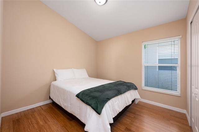 bedroom with vaulted ceiling, wood finished floors, and baseboards