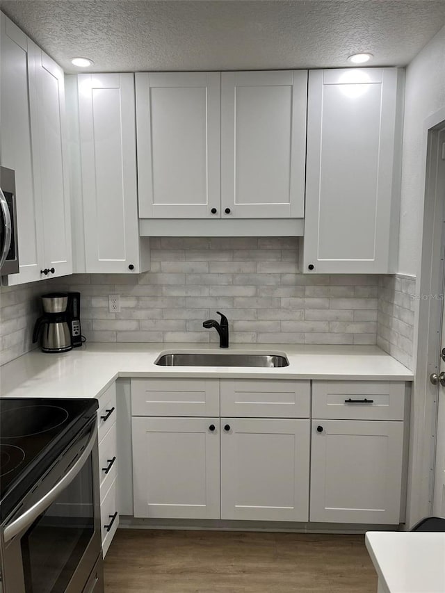 kitchen with wood-type flooring, sink, white cabinets, and a textured ceiling