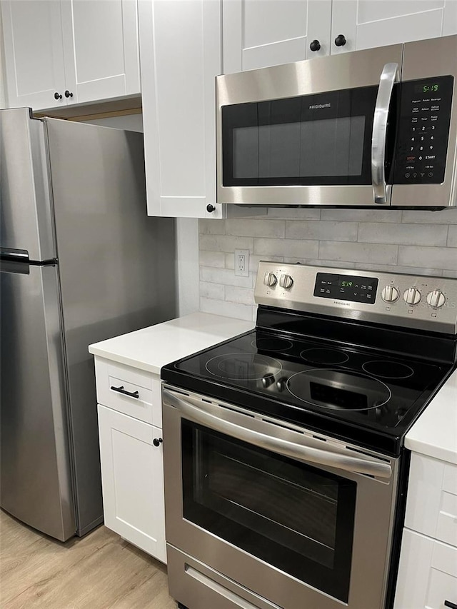 kitchen with stainless steel appliances, white cabinets, backsplash, and light hardwood / wood-style flooring