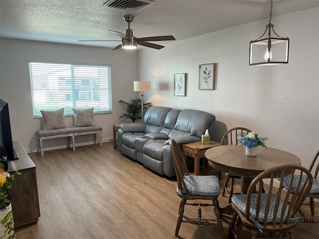 living room with ceiling fan, light hardwood / wood-style flooring, and a textured ceiling