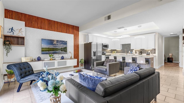 living room featuring sink, light tile patterned floors, and a tray ceiling