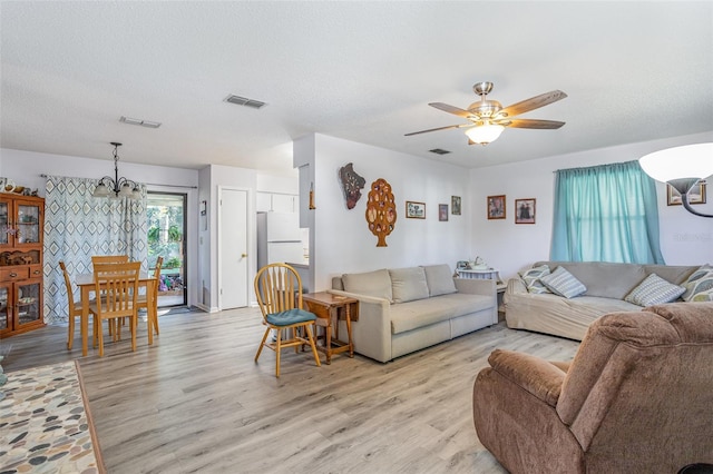 living area with light wood-style flooring, visible vents, a textured ceiling, and ceiling fan with notable chandelier