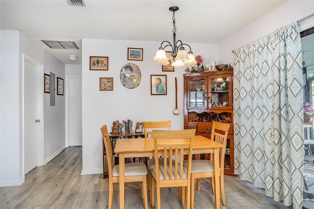 dining room with a textured ceiling, a notable chandelier, visible vents, baseboards, and light wood-style floors