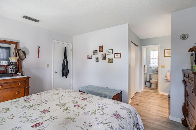 bedroom with a textured ceiling, connected bathroom, light wood-style flooring, visible vents, and baseboards