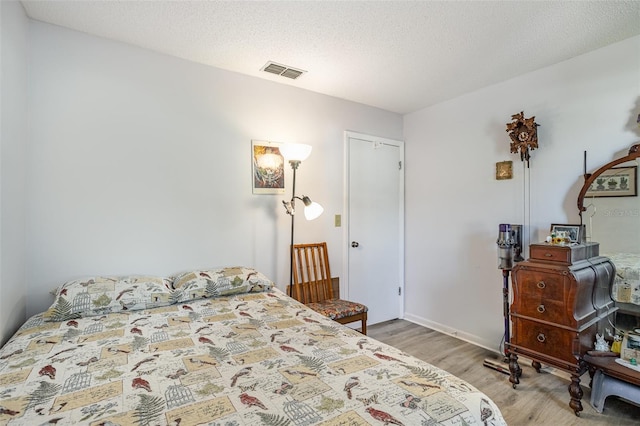 bedroom with a textured ceiling, visible vents, and wood finished floors