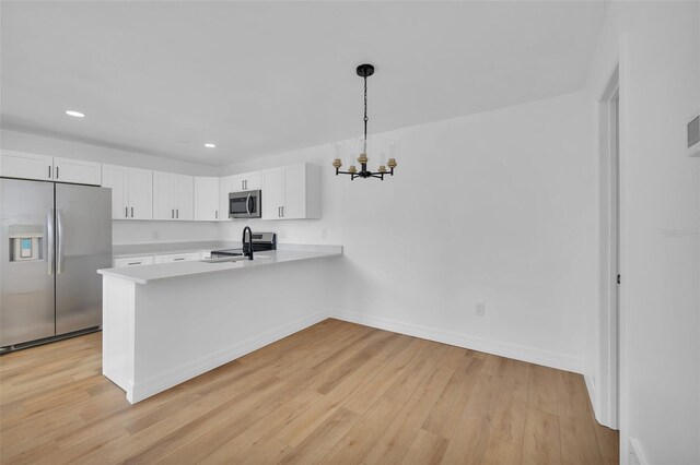 kitchen with decorative light fixtures, kitchen peninsula, stainless steel appliances, light hardwood / wood-style floors, and white cabinets