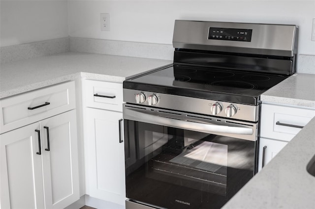 kitchen featuring electric stove, light stone counters, and white cabinets