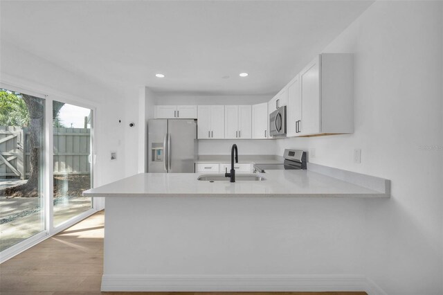 kitchen featuring stainless steel appliances, kitchen peninsula, sink, and white cabinets