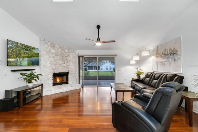 living area featuring ceiling fan, a stone fireplace, vaulted ceiling, and wood finished floors