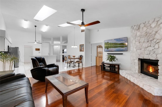 living room featuring light wood-type flooring, ceiling fan, a stone fireplace, and a skylight