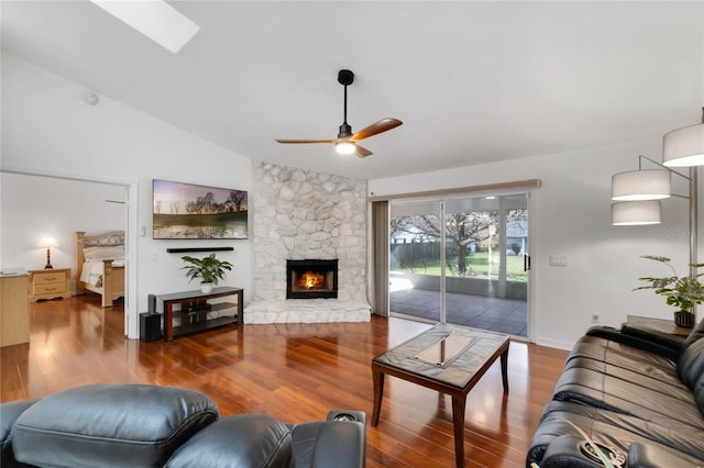 living area with lofted ceiling with skylight, ceiling fan, wood finished floors, and a stone fireplace