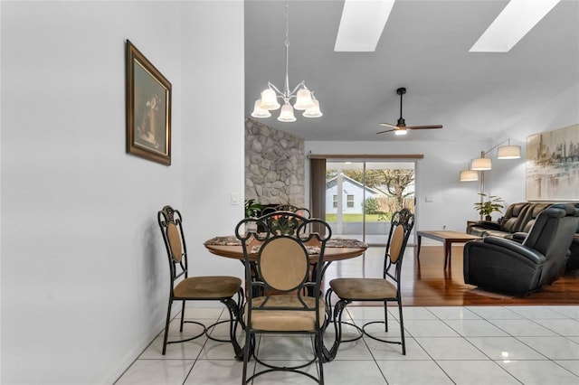 dining area featuring a skylight, a fireplace, light tile patterned floors, baseboards, and ceiling fan with notable chandelier