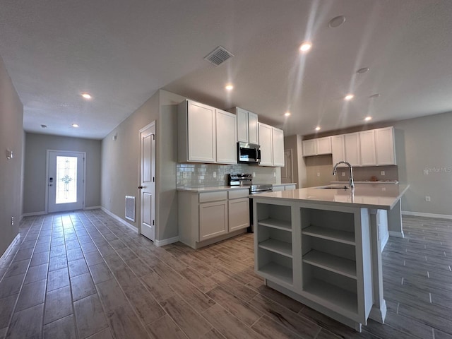 kitchen with sink, white cabinetry, stainless steel appliances, a center island with sink, and decorative backsplash