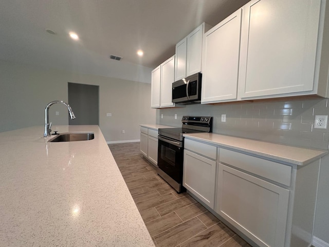 kitchen with sink, stainless steel appliances, tasteful backsplash, wood-type flooring, and white cabinets