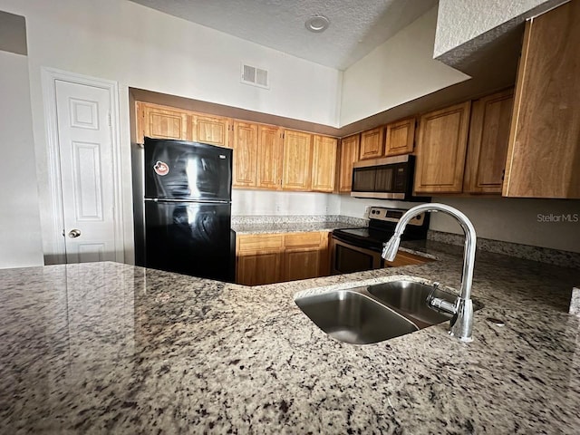 kitchen featuring appliances with stainless steel finishes, sink, a textured ceiling, and light stone counters