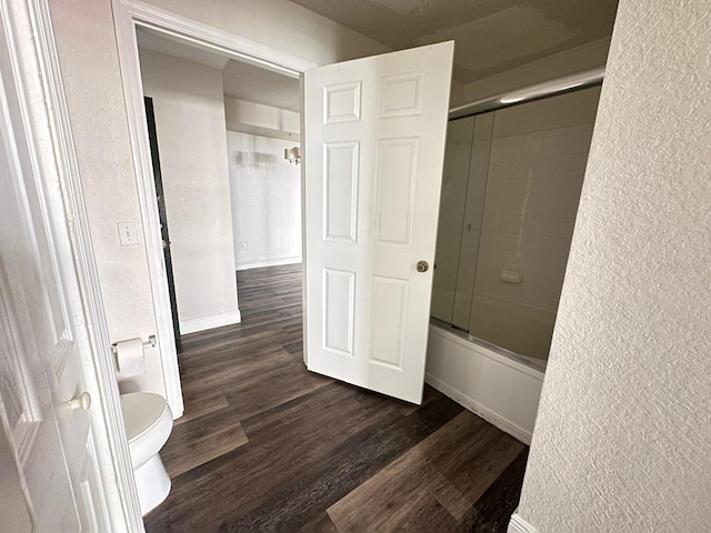 bathroom with hardwood / wood-style flooring, enclosed tub / shower combo, and toilet