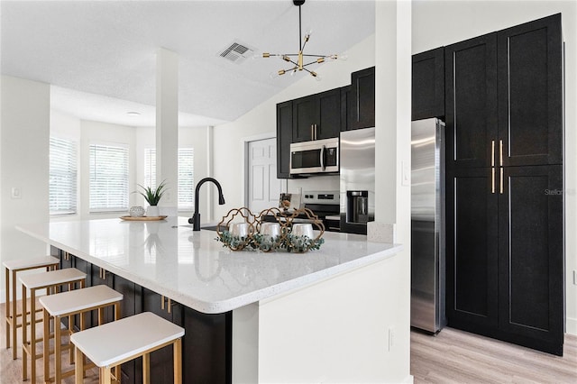 kitchen with light stone countertops, an island with sink, appliances with stainless steel finishes, and pendant lighting