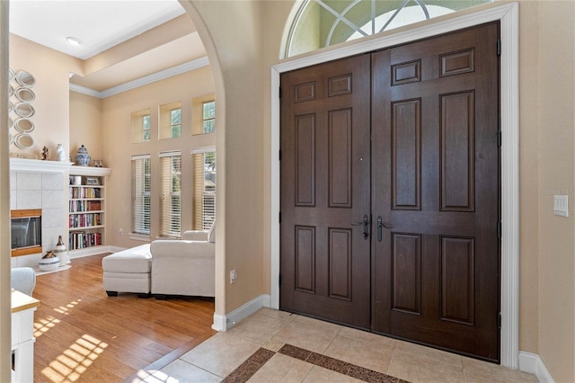 entryway with ornamental molding, light hardwood / wood-style flooring, a tile fireplace, and a high ceiling