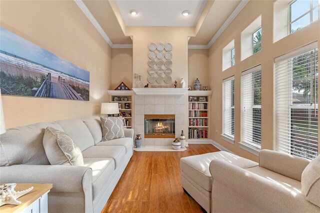 living room featuring crown molding, a tray ceiling, a tiled fireplace, and hardwood / wood-style floors