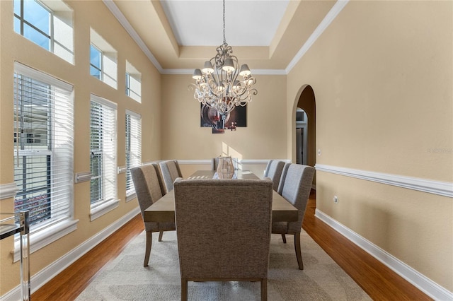 dining space featuring a high ceiling, hardwood / wood-style floors, an inviting chandelier, and a tray ceiling