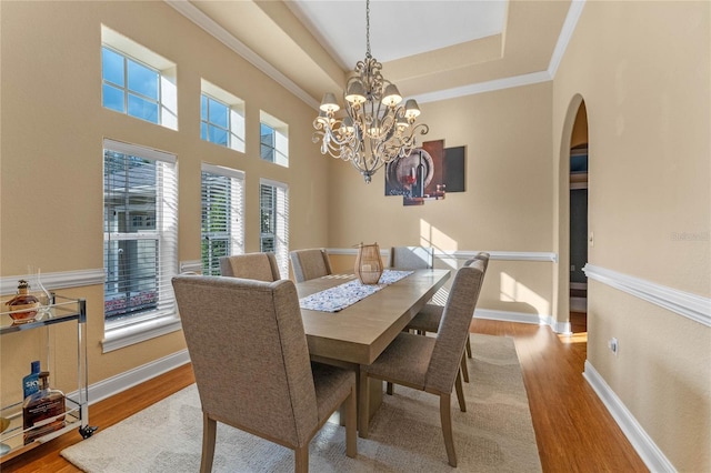 dining area with crown molding, a chandelier, light wood-type flooring, and a tray ceiling