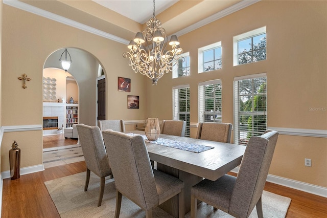 dining area featuring a notable chandelier, a tray ceiling, a fireplace, wood-type flooring, and ornamental molding