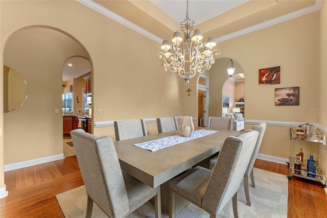 dining room with an inviting chandelier, ornamental molding, wood-type flooring, and a raised ceiling