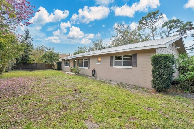 back of property featuring metal roof, fence, and a lawn