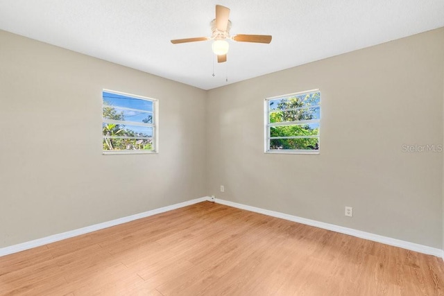 spare room featuring plenty of natural light, light wood-type flooring, baseboards, and a ceiling fan
