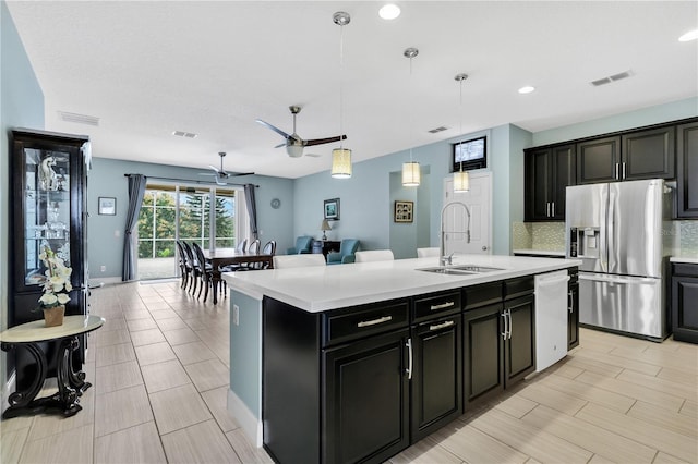 kitchen with sink, stainless steel fridge, backsplash, a center island with sink, and decorative light fixtures