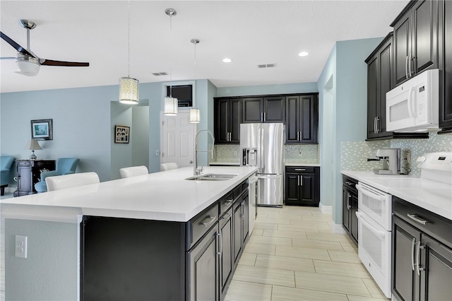 kitchen with appliances with stainless steel finishes, sink, a kitchen bar, hanging light fixtures, and a center island with sink