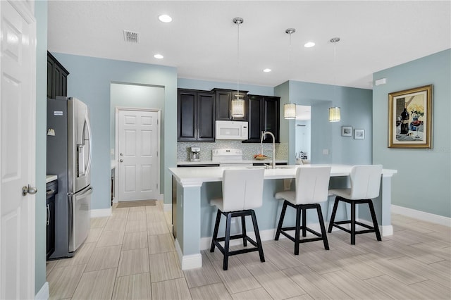 kitchen featuring sink, white appliances, a kitchen island with sink, backsplash, and decorative light fixtures