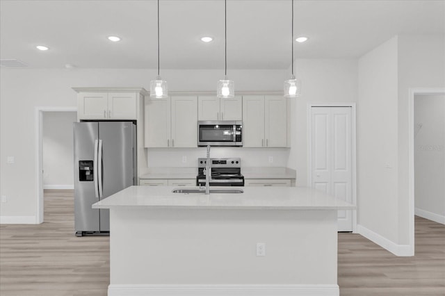 kitchen with stainless steel appliances, white cabinetry, an island with sink, and decorative light fixtures