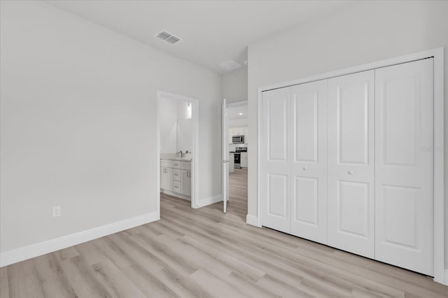 unfurnished bedroom with connected bathroom, sink, a closet, and light wood-type flooring