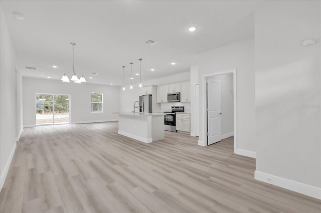 kitchen with white cabinetry, appliances with stainless steel finishes, an island with sink, pendant lighting, and light hardwood / wood-style floors