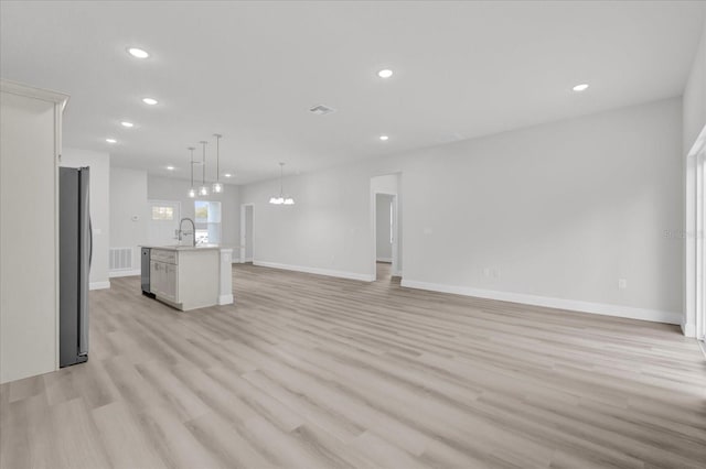 unfurnished living room featuring an inviting chandelier, sink, and light hardwood / wood-style flooring