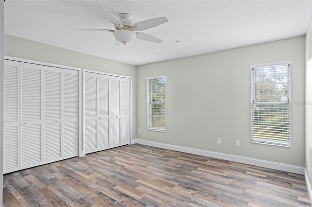 unfurnished bedroom with two closets, wood-type flooring, a textured ceiling, and ceiling fan